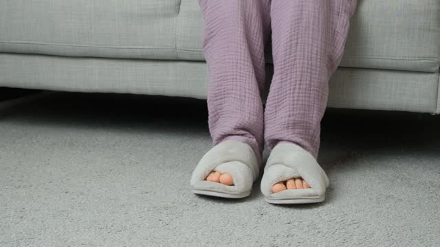 Woman in pajamas and slippers sitting on sofa in contemplation.