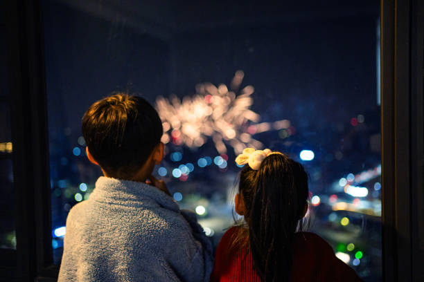 Setting off fireworks outside the window，The siblings are watching the fireworks outside the window at home