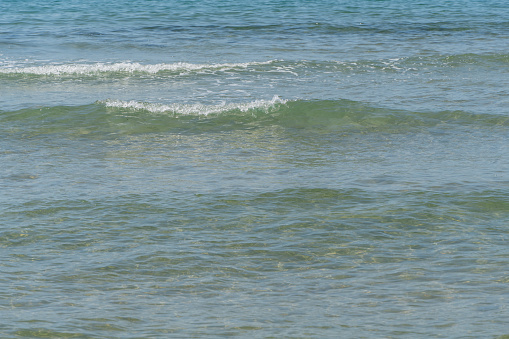 White waves rolls on sandy shore of Black Sea Anapa. White splashes and foam in foreground. Emerald-blue transparent sea water washes yellowish sand. Sea at southern resort of Russia.