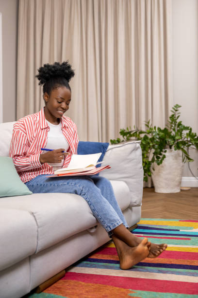 istock Woman writing to do list or plan for day while sitting on couch in home interior. 1924942088