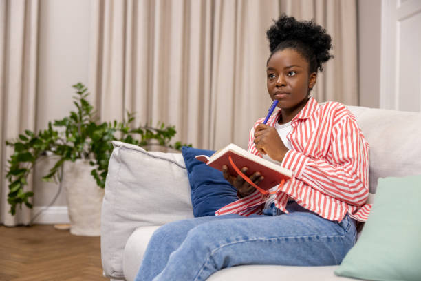 istock Woman writing to do list or plan for day while sitting on couch in home interior. 1924942094