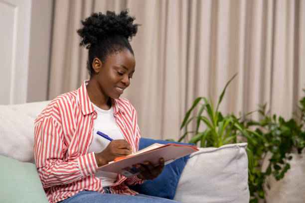 istock Woman writing her personal notes into her diary while sitting on sofa in living room. 1924942102