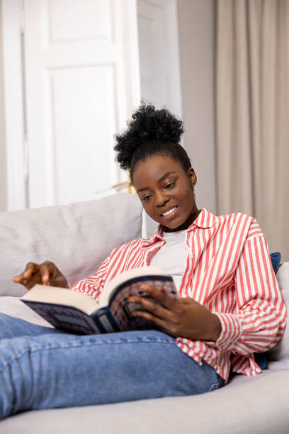 istock Smiling woman reading book while sitting on sofa at home. 1924942644