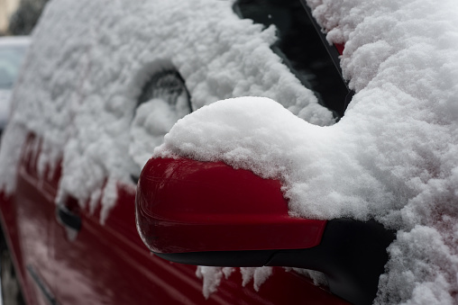 Closeup of red mirror of car covered by the snow parked in the street