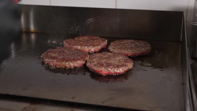 A close-up of the chef frying meat patties and turning them over with a spatula.