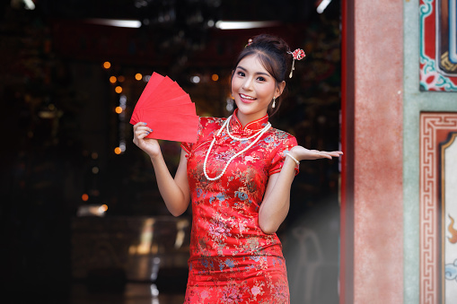 Concept to celebrate Chinese New Year : Chinese woman in a red cheongsam (qipao) dress holding red envelopes (hong bao) at shrine.