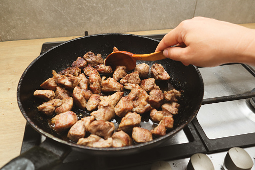 Woman mixing the meat in a frying pan shovel. Pan-fried meat, French fries. Close up of a pan with preparing of beef stroganoff