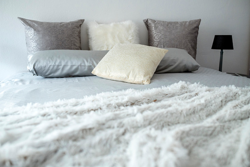 A bed with a cosy fur blanket and various pillows.