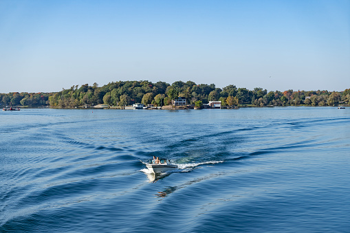 One of the thousand islands near Gananoque on Lake Ontario.  There is a leisure boat with people on it in the foreground.