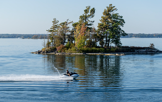 One of the thousand islands near Gananoque on Lake Ontario.  There is a jet skier beside the tour boat.