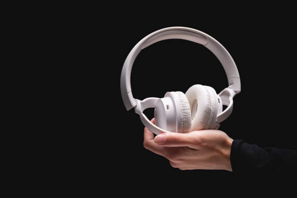 istock Wireless headphones on a black background. White full-size noise-canceling headset with built-in microphone. Side view of acoustic stereo sound system in female hand 1925017736