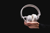 Wireless headphones on a black background. White full-size noise-canceling headset with built-in microphone. Side view of acoustic stereo sound system in female hand