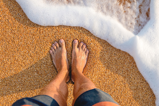 Young man standing on the beach sand on a hot summer day in Thasos, Greece. His POV.