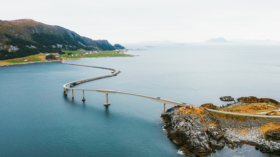 High-angle panoramic photo of vehicles on idyllic road above the sea between the small Norwegian towns on the island during summer in Scandinavia