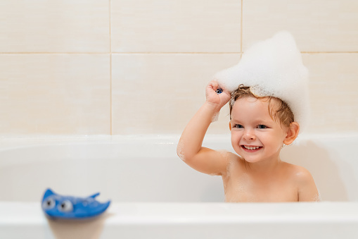 Funny little boy taking a bath with foam hat and blue stingray toy. Copy space