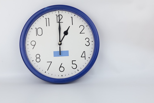 Blue alarm clock on white table in front of blue colored wall. The clocks time is showing 5 to 12.