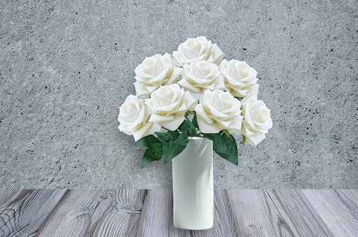 Bouquet of white roses in a vase on a wooden table. Against the background of a concrete gray wall.