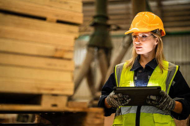 istock woman worker carpenter wearing safety uniform and hard hat working and checking the quality of wooden products at workshop manufacturing. man and woman workers wood in dark warehouse industry. 1925134117