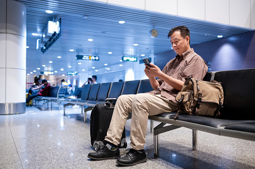 Asian male entrepreneur checking travel information on electronic boarding pass using smart phone before boarding the flight.