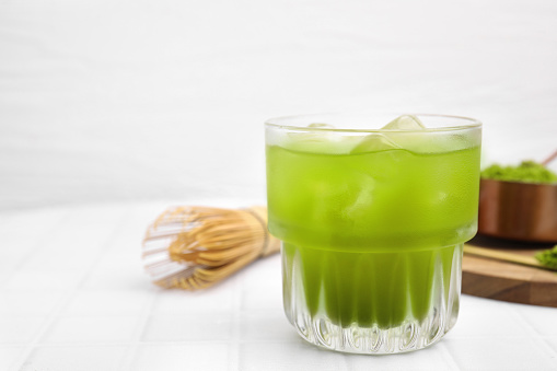 Glass of delicious iced green matcha tea on white tiled table, closeup. Space for text