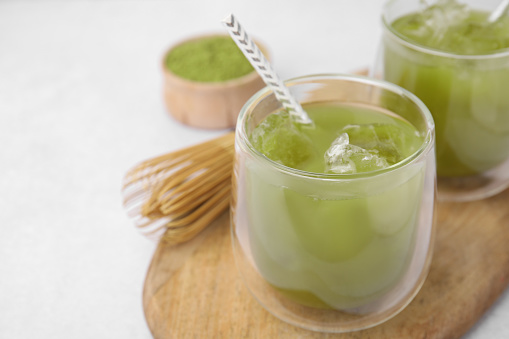 Delicious iced green matcha tea and bamboo whisk on white table, closeup. Space for text