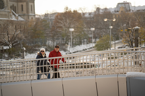 senior couple, tourists walking up bridge for pedestrians in snowy city on cold day in winter