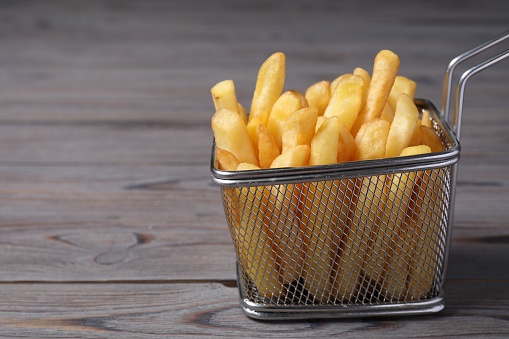 Metal basket with tasty French fries on grey wooden table, closeup. Space for text