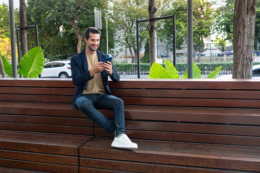 Happy Latin American businessman with formalwear chatting with his customer while sitting on a wooden bench for showing the support of the flexible working environment.