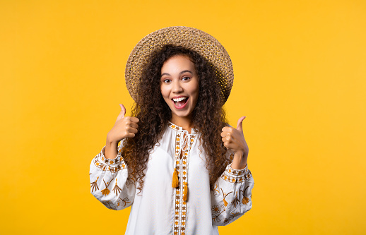 Positive ukrainian woman makes like hand sign, thumbs up gesture. Happy girl, correct perfect choice, great deal, yellow background. Positive lady smiles to camera, approval, trust concept.