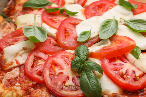 Delicious Caprese pizza with tomatoes, mozzarella and basil as background, closeup