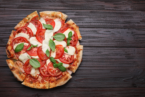 Delicious Caprese pizza with tomatoes, mozzarella and basil on dark wooden table, top view. Space for text