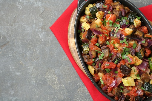 Dish with tasty ratatouille on grey textured table, top view. Space for text