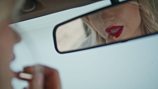 istock Car mirror reflecting beautiful woman applying red lipstick on lips close up. 1925227182