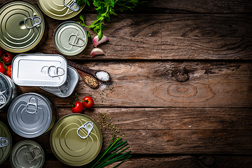 Overhead view of metal tins of food of different sizes, colors and shapes shot at the left of a dark wooden table. Copy space. High resolution 42Mp studio digital capture taken with Sony A7rII and Sony FE 90mm f2.8 macro G OSS lens
