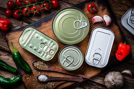 Overhead view of four metal tins of food of different sizes, colors and shapes shot on dark wooden table. High resolution 42Mp studio digital capture taken with Sony A7rII and Sony FE 90mm f2.8 macro G OSS lens
