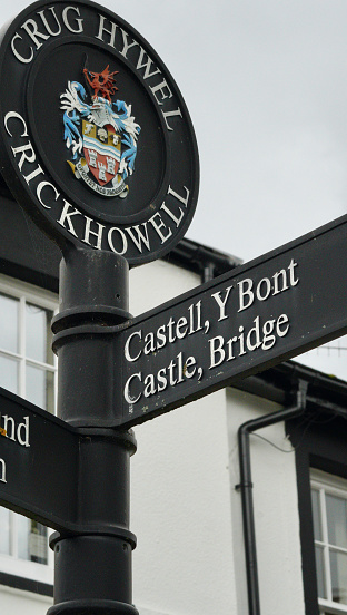 Colourful bilingual sign in Crickhowell, Crug Hywel, with the welsh town's coat of arms and crest with pointers for visitors to places of interest such as Castell y bont, translated as Castle Bridge.