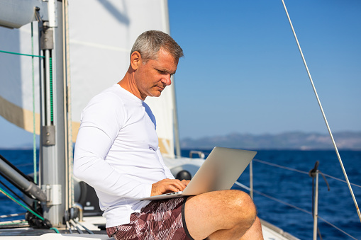 Businessman using laptop computer on sailboat.