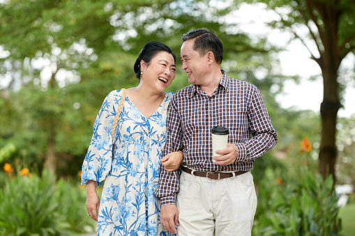 Cheerful senior woman laughing at joke of husband when they are walking in city park