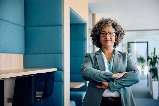 Happy mature CEO standing with her arms crossed in the office and looking at camera.