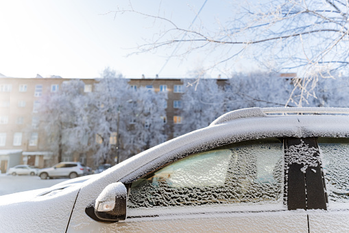 A car covered with snow is parked near the house, the side window of the car is frozen. High quality photo
