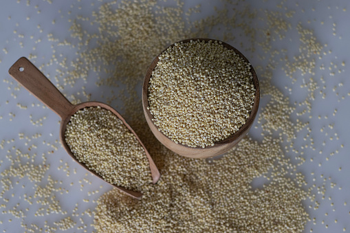 Close up of wholesome proso millet, presented in a rustic wooden bowl, surrounded by scattered golden millet grains on a wooden grain spoon. A wholesome and nutritious agricultural concept