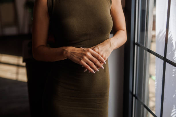 Midsection of unrecognizable woman standing by the window, looking outside, daydreaming.