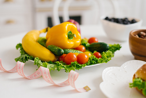 Vegetables and fruits for weight loss on a plate with a measuring tape in the kitchen