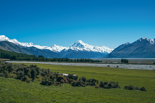 Discover the picturesque landscape in New Zealand's South Island leading to the renowned Mount Cook mountain. Behold the stunning sight of snow-capped Mount Cook, majestically framed by other towering mountain peaks.