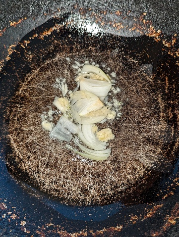 Chopped garlic and onion being sauteed and cooked in grapeseed oil in a pot which is on a stove's flame.