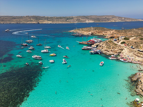 Sun-soaked Bliss: Aerial view of Comino's Blue Lagoon, Malta, on a scorching hot summer day by the Mediterranean Sea. People sunbathing and boats resting on the water surface.