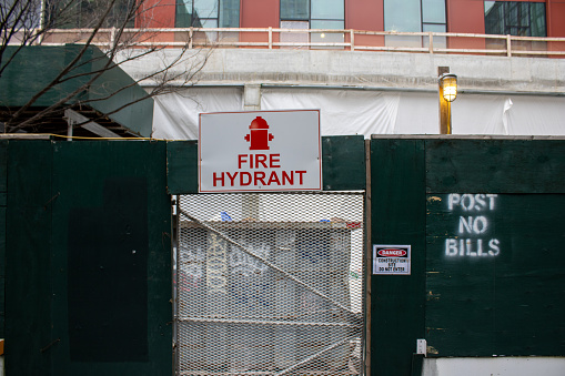 Nyc, United States – January 07, 2024: A vivid red sign is attached to a metal gate, directly above a bright yellow fire hydrant