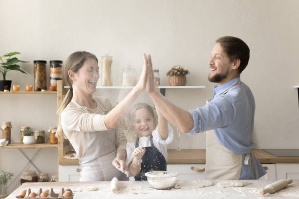 Cheerful mom, dad and little daughter baking in home kitchen
