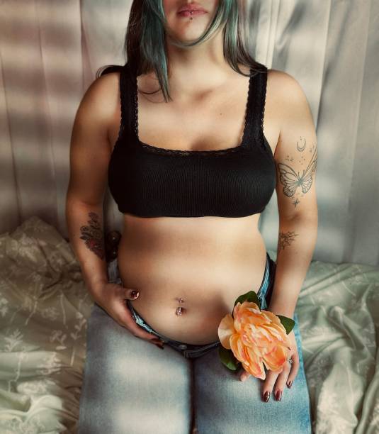 花を持つ妊娠中の若い成人女性の不機嫌な肖像画。 - pierced abdomen flower beauty ストックフォトと画像