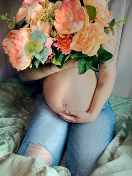 花を持つ妊娠中の若い成人女性の不機嫌な肖像画。 - pierced abdomen flower beauty ストックフォトと画像